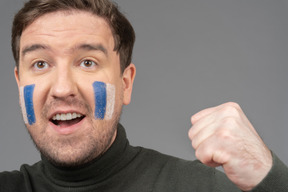 Un retrato de un fanático del fútbol masculino con arte de cara azul y blanca apretando el puño