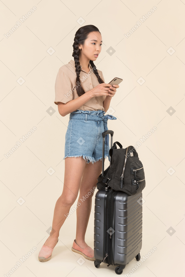 Female traveler looking away while holding her smartphone