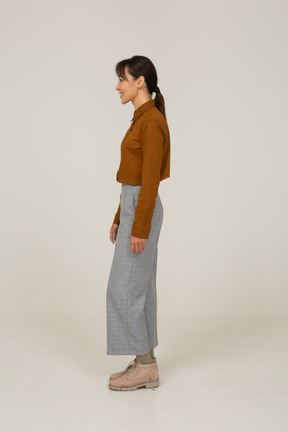 Side view of a smiling young asian female in breeches and blouse standing still