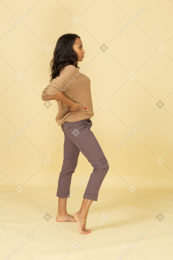 一个专横的深色皮肤的年轻女性，将手放在臀部上的侧视图