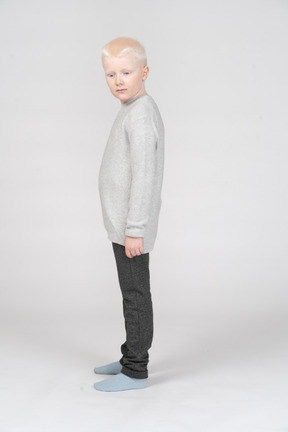A blonde little boy in casual clothes standing thoughtfully