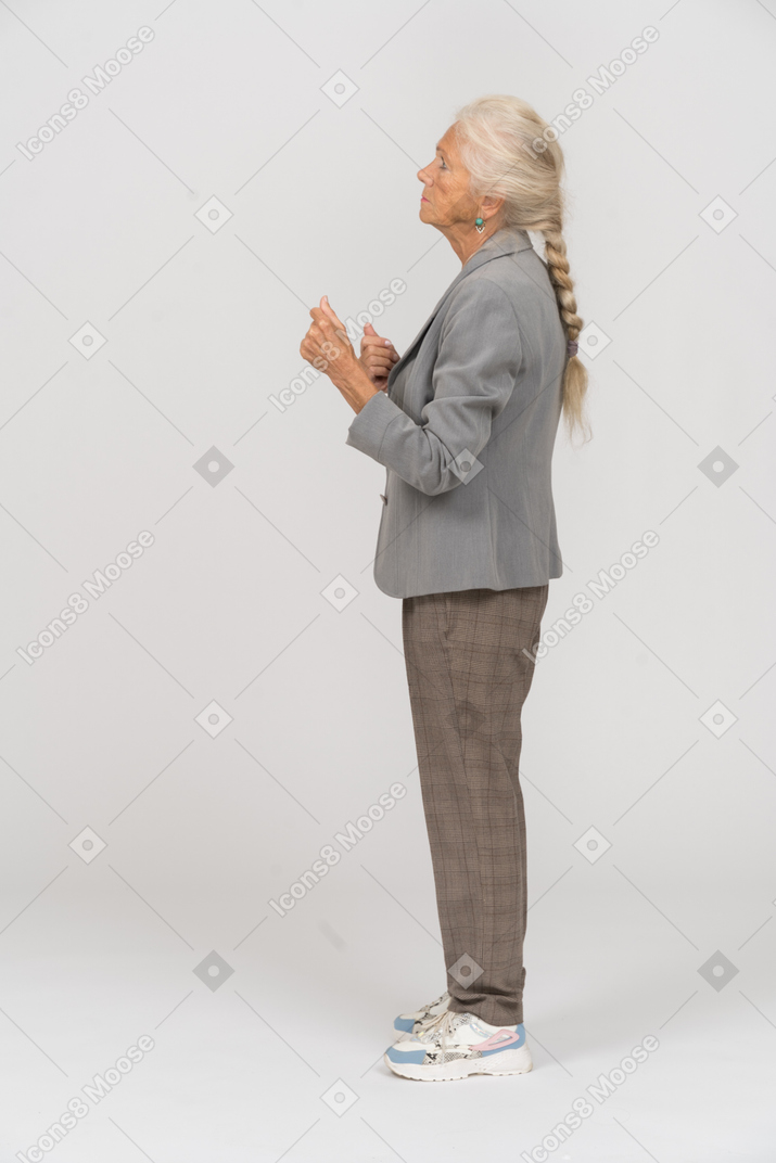 一位身着西装的老妇人握紧拳头站立的侧视图