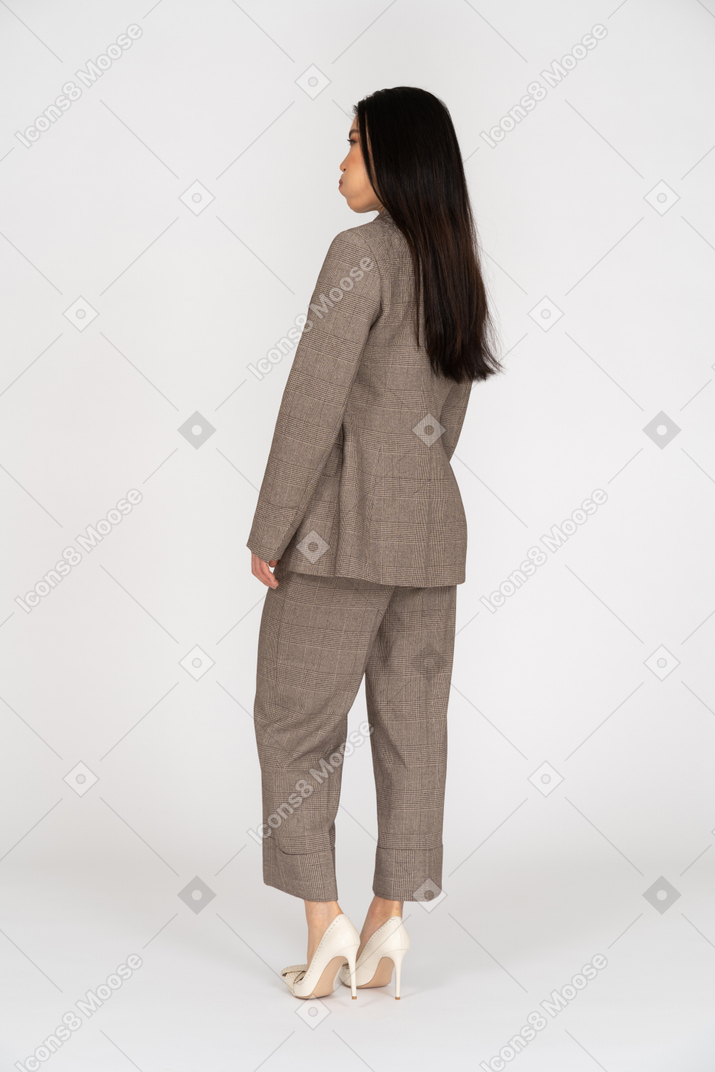 頬を吹く茶色のビジネススーツの若い女性の4分の3の背面図