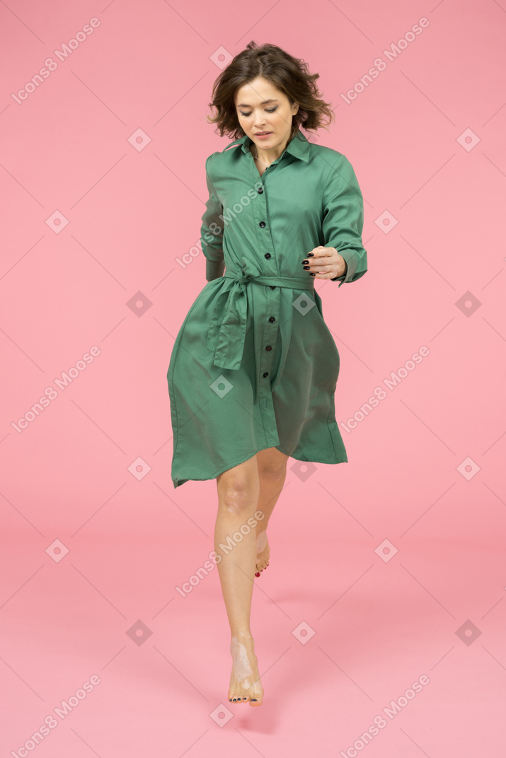 Alegre jovencita en vestido verde dando pasos seguros hacia adelante