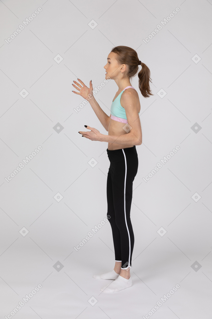 Side view of a teen girl in sportswear raising hands and looking aside