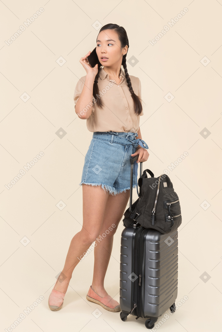 電話で話しているスーツケースを持つ若い女性