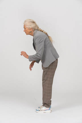 Vista lateral de uma senhora idosa de terno curvando-se e mostrando a placa de pare