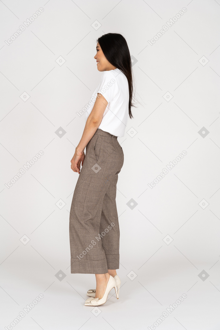 Vista lateral de uma jovem tímida e sorridente de calça e camiseta de mãos dadas