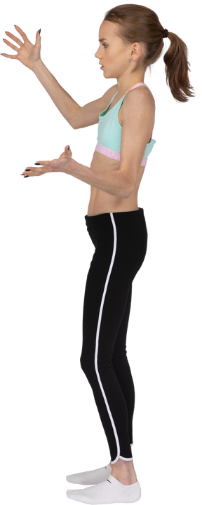 Three-quarter back view of an astonished teen girl in sportswear raising hands