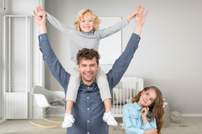 A man is holding a boy on his shoulders while a girl is looking at them wistfully