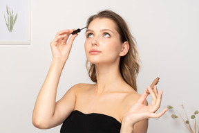 Three-quarter view of a young woman wearing black top holding brushing her eyebrows