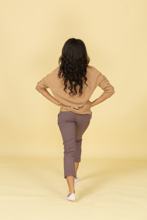 Back view of a squatting dark-skinned young female making a lunge