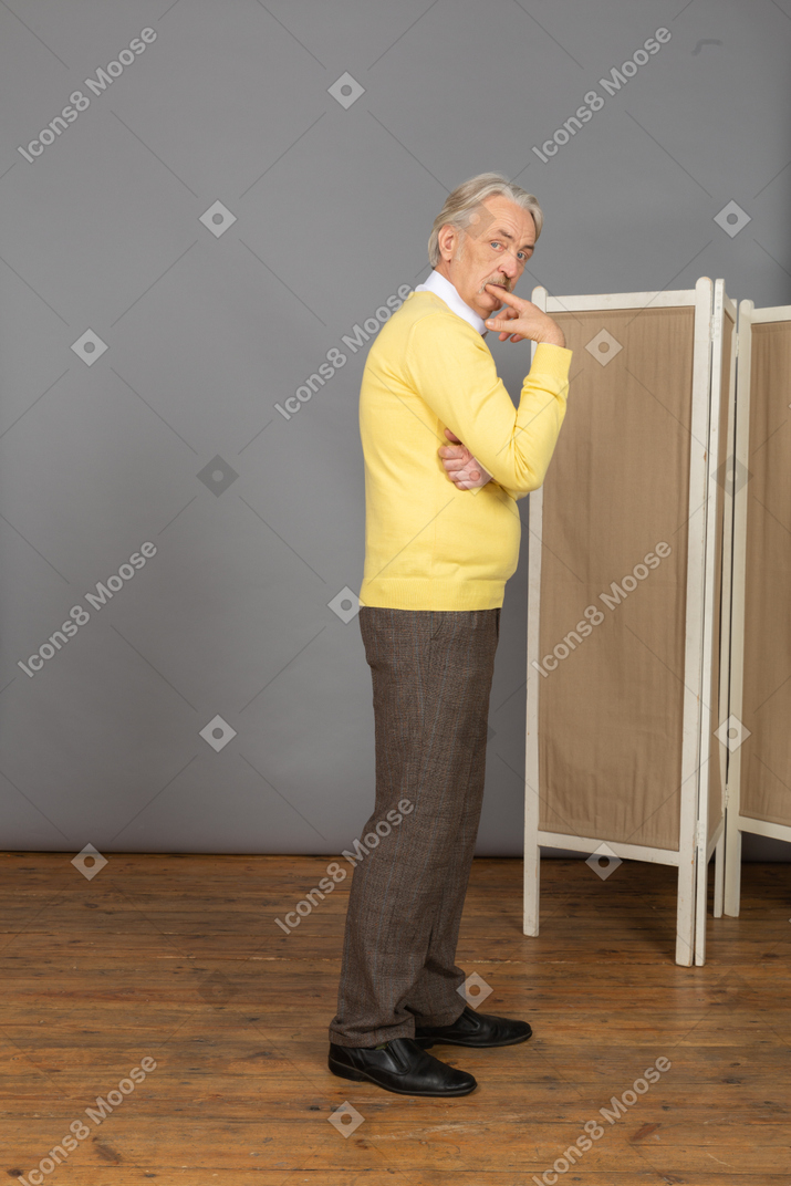Side view of an old man biting finger while looking at camera