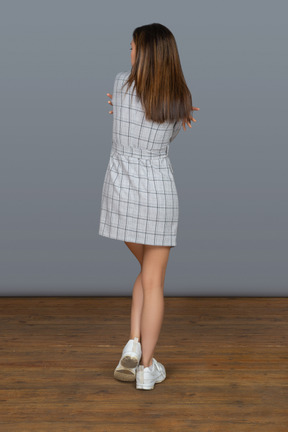 Unrecognizable slim woman with long brown hair standing back to camera and embracing herself