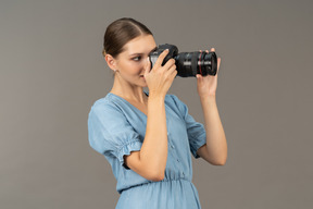 Three-quarter view of a smiling young woman in blue dress taking shot