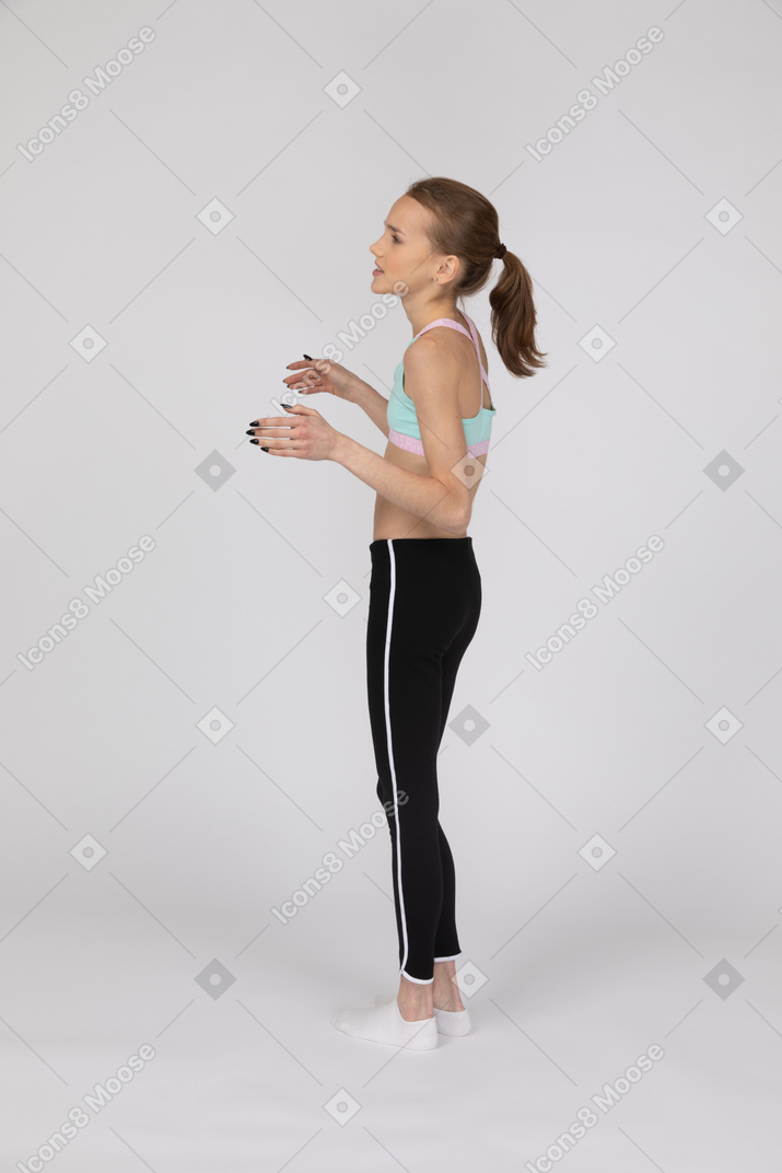 Vista laterale di una ragazza adolescente perplessa in abiti sportivi alzando le mani