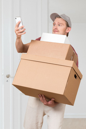 A man holding a cardboard box and a cell phone