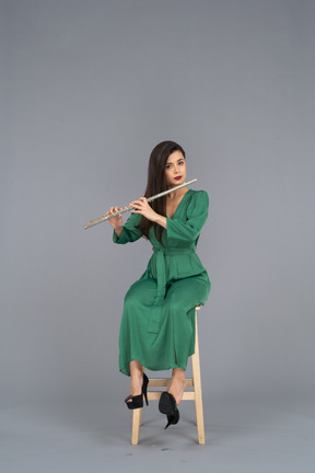 Front view of a young lady in green dress sitting on a chair while playing the clarinet