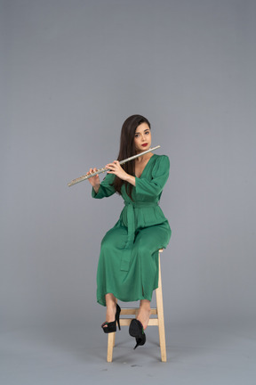 Vista frontal de uma jovem de vestido verde sentada em uma cadeira enquanto toca clarinete