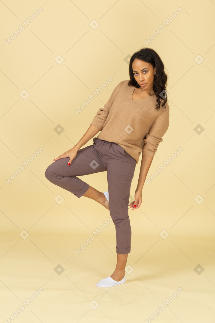 Vista de tres cuartos de una mujer joven de piel oscura levantando la pierna mientras se inclina hacia atrás