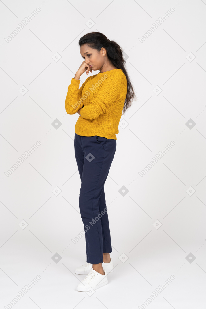 Vista lateral de uma garota entediada em roupas casuais, segurando o punho na bochecha e olhando para baixo