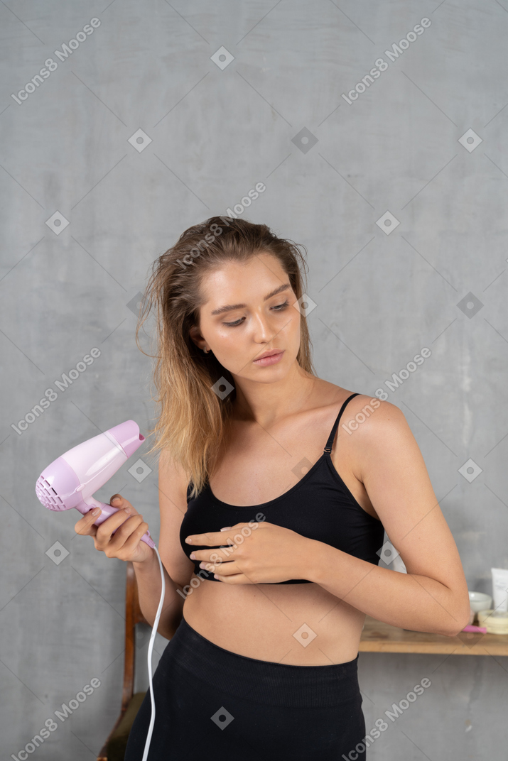 Front view of a young woman blow-drying her hair