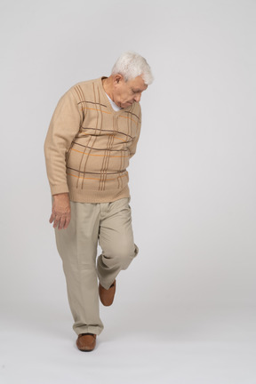 Front view of an old man in casual clothes standing on one leg and looking down