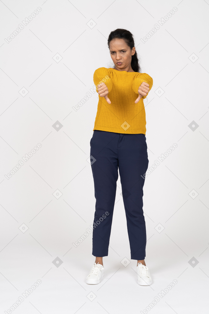 Front view of an upset girl in casual clothes showing thumbs down and looking at camera