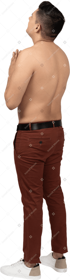 Vista posteriore di tre quarti di un uomo latino a torso nudo che si stringe le mani e guarda in alto