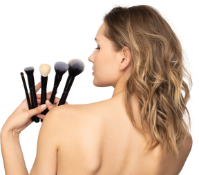 Back view of a sensual young woman holding make-up brushes