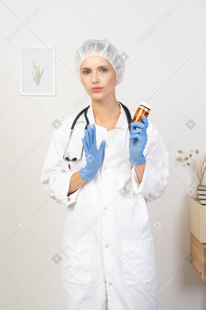 Front view of a young female doctor holding a jar of pills