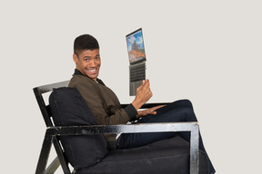 Vista lateral de um jovem sentado em um sofá segurando um laptop