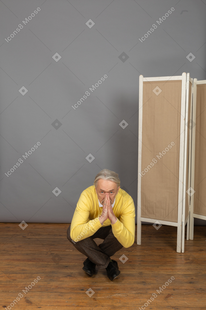 Front view of a squatting old man showing a namaste sign