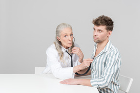 Aged female doctor examining a patient with a stethoscope