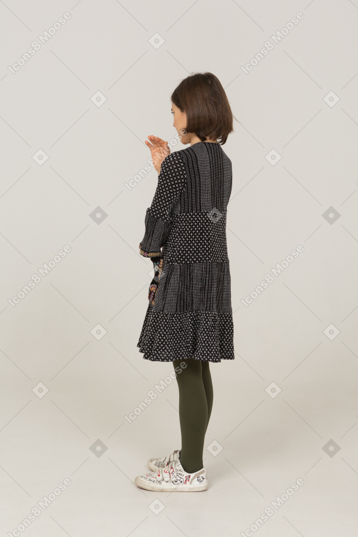 Vista posterior de tres cuartos de una niña vestida explicando algo y levantando la mano
