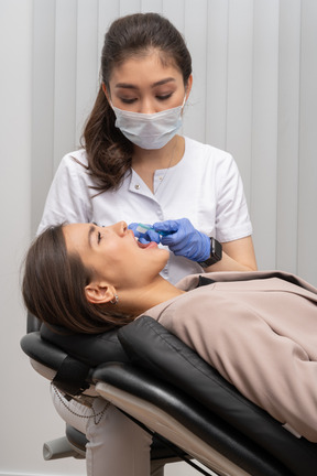 A female dentist holding a toothbrush and a female patient lying with her mouth open
