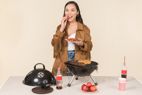 Young asian woman standing near grill and throwing a fruit