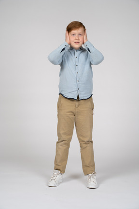 Vista frontal de um menino cobrindo os ouvidos com as mãos e olhando para a câmera