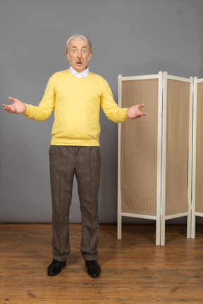 Front view of an astonished old man near the screen raising hands