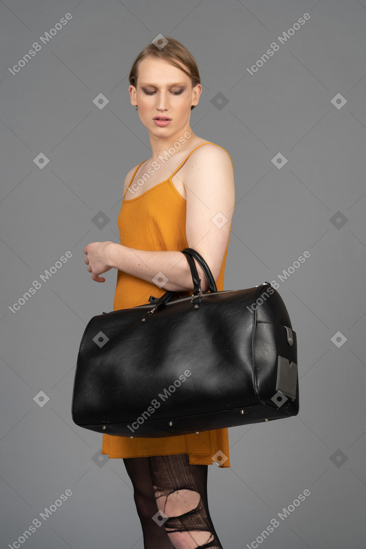 Vista lateral de um jovem de vestido laranja carregando bolsa de couro