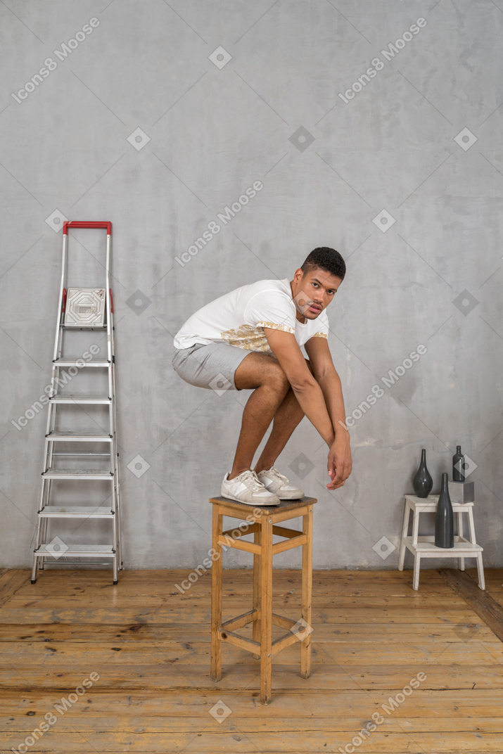 Молодой человек стоит на стуле с согнутыми коленями