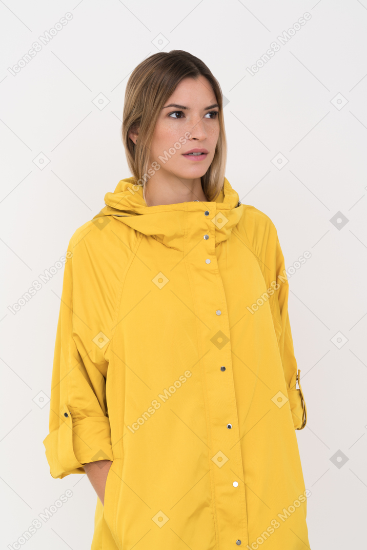 Женщина в желтоватом плаще смущенно смотрит на что-то