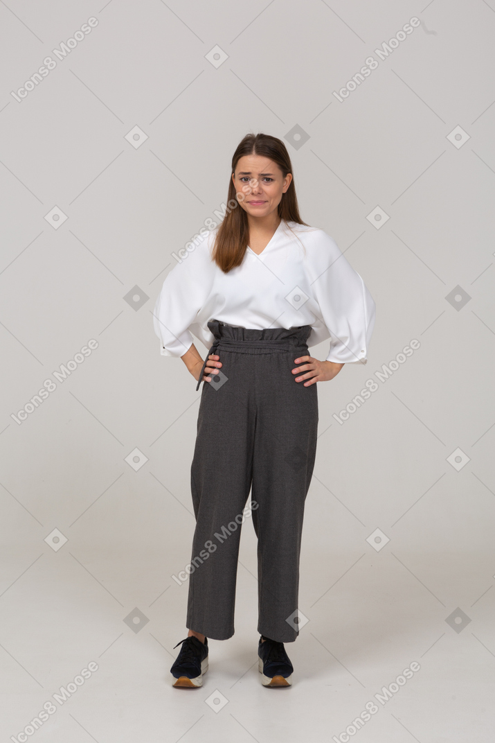 Vue de face d'une jeune femme confuse en vêtements de bureau mettant les mains sur les hanches