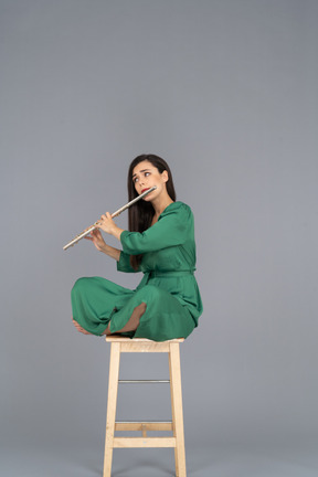 Comprimento total de uma jovem tocando clarinete sentada com as pernas cruzadas em uma cadeira de madeira