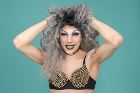 Drag queen con un reggiseno borchiato che si scompiglia i capelli