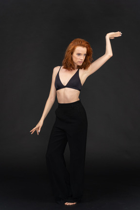 A frontal view of the young cute woman standing on the black background dancing and looking to the right