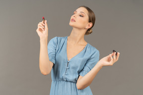 Front view of a young woman in blue dress holding a lipstick