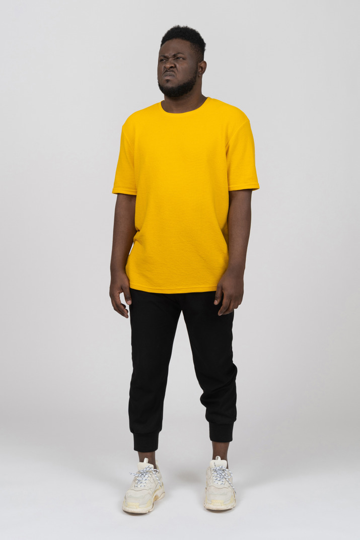 Front view of a displeased grimacing young dark-skinned man in yellow t-shirt