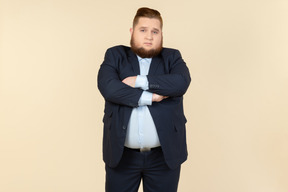 Offended looking young overweight office employee standing with his hands crossed
