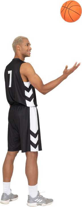 Dreiviertel-rückansicht eines lächelnden jungen männlichen basketballspielers, der einen ball wirft